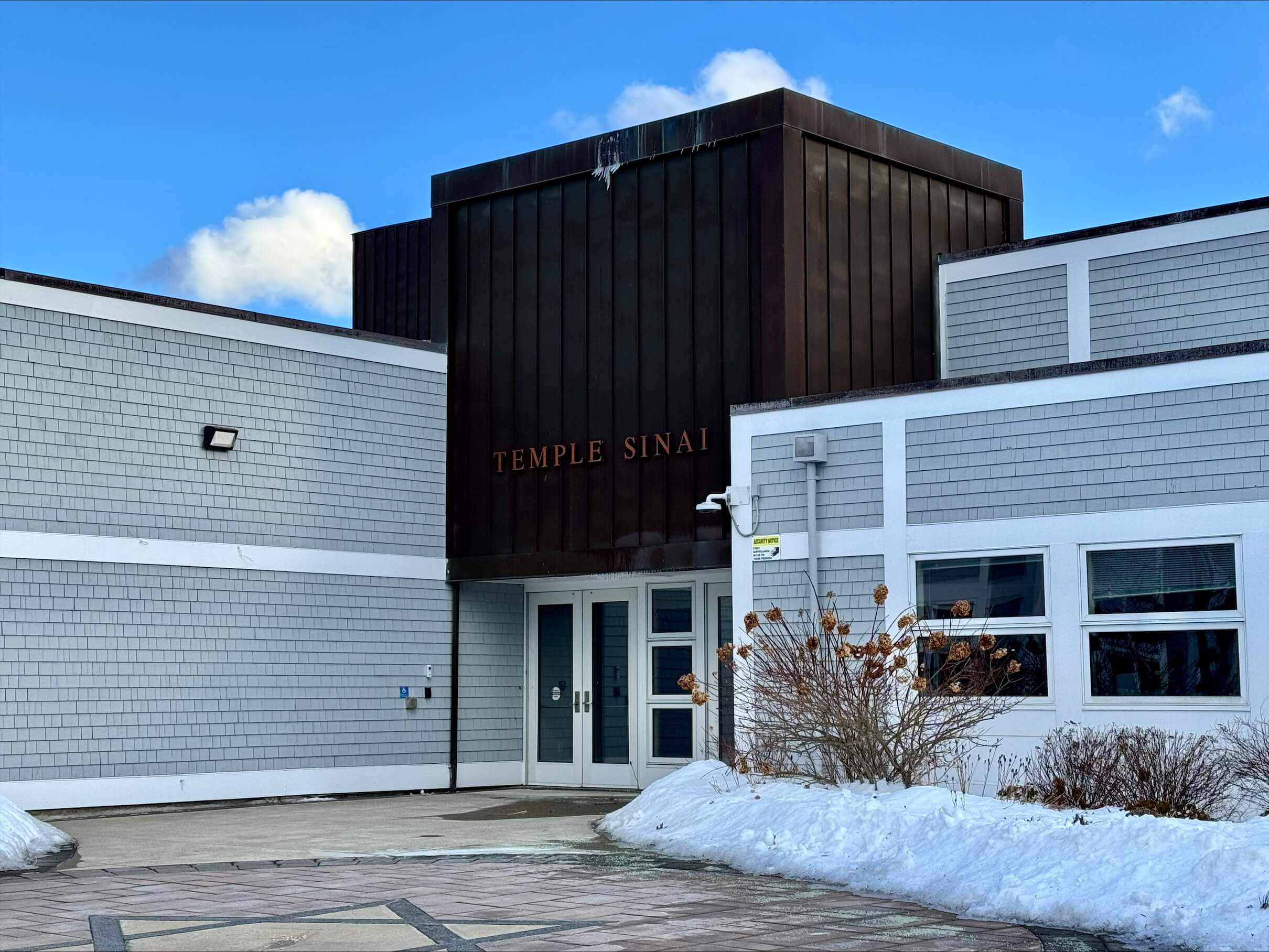 An exterior photo of Temple Sinai in Sharon MA with show pilled up to the sides of the main walkway, which features a Star of David.